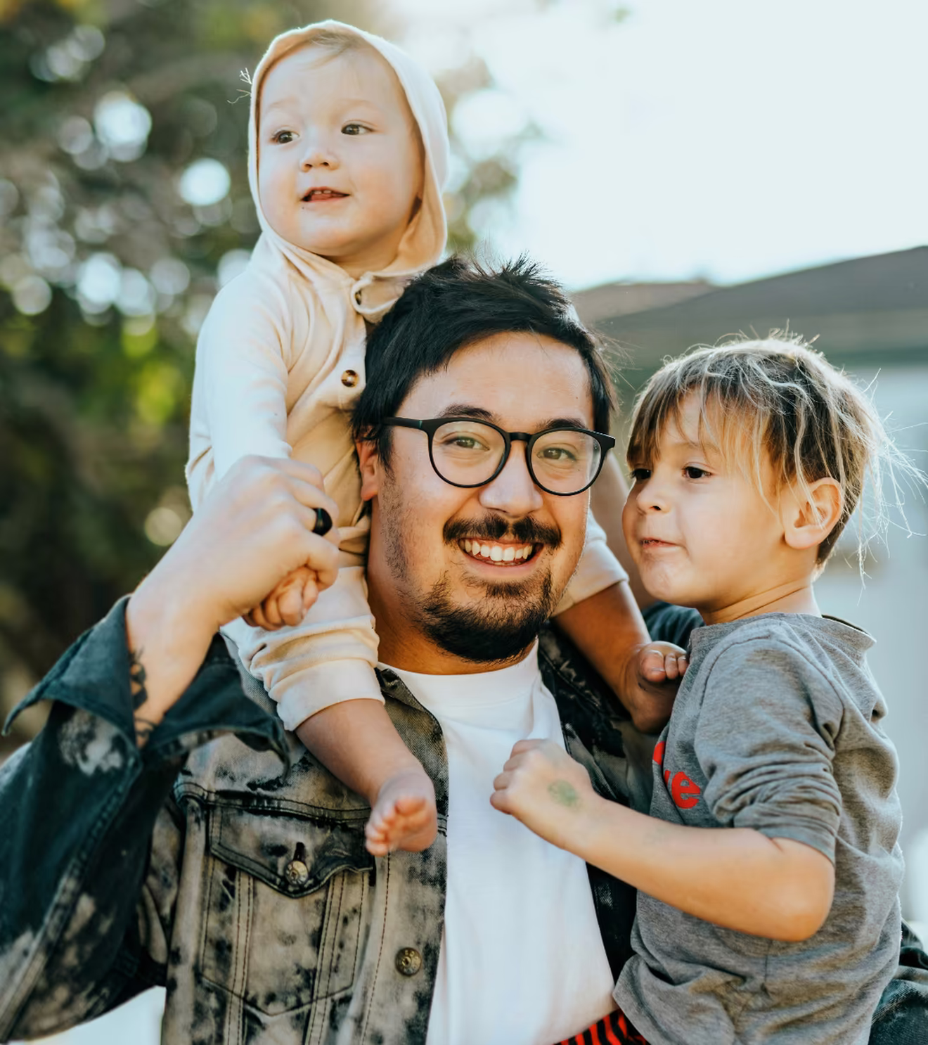 Father with a baby on his shoulder and a toddler in his arm beside a white picket fence