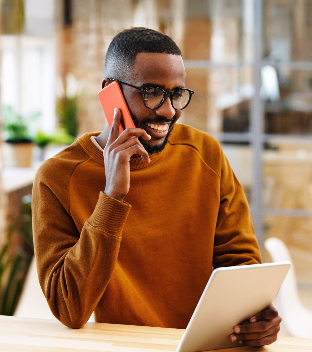 Man smiling on a phone call at a sunny desk, tablet in hand