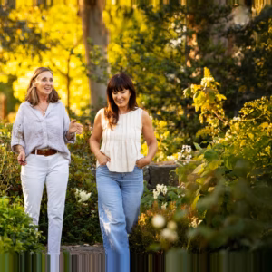 Two women walking and talking together through a sunlit garden